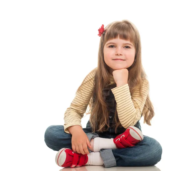 Cute little girl wearing jeans overall sitting on the floor and — Stock Photo, Image