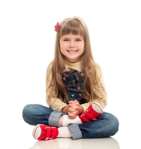 Cute little girl wearing jeans overall sitting on the floor and — Stock Photo, Image