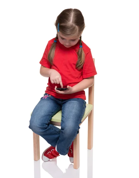Маленька дівчинка сидить на стільці і використовує смартфон — стокове фото
