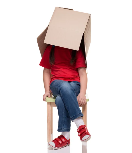 Bambino seduto su una sedia con grande scatola coperta testa — Foto Stock