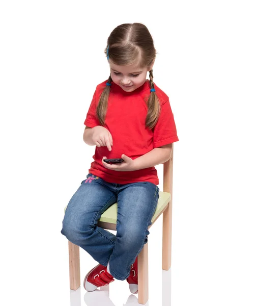 Niña sentada en una silla y usando un teléfono inteligente — Foto de Stock