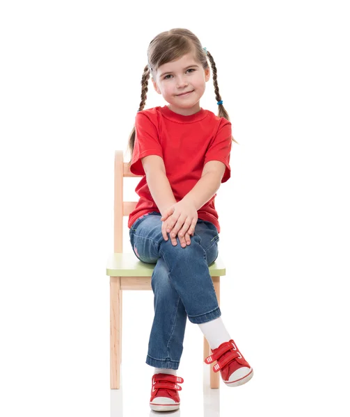 Liten flicka klädd i röd t-shirt och poserar på stol — Stockfoto