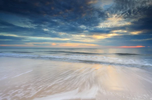 Prachtige zonsondergang op het strand met golven stroomt over Stockfoto