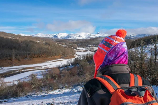 一个带着帽子和背包的女登山者看着白雪覆盖的高山 — 图库照片