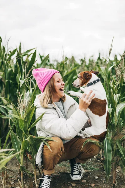 幸せな十代の女の子抱擁彼女の犬ジャックラッセルテリアでフィールドに背景にコーンフィールドで秋 — ストック写真