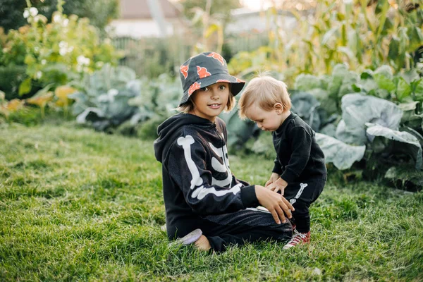 Ein glücklicher blonder Junge und seine Schwester in Karnevalskostümen spielen an Halloween im Garten — Stockfoto
