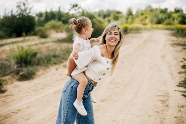 Mutlu bir anne ve küçük bir kız birlikte oynuyorlar, bir kız annesinin sırtında.