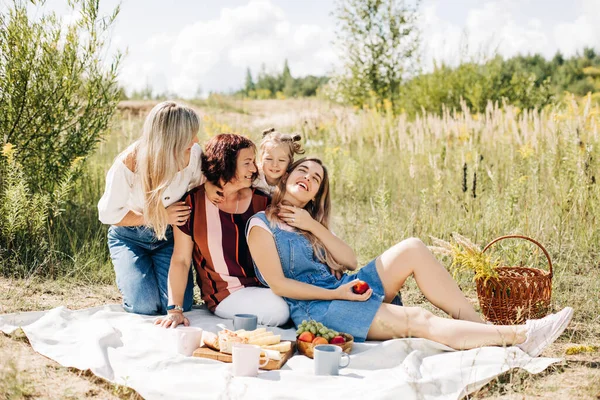 Rodina pořádá piknik na trávníku. Tři generace žen stejné rodiny odpočívají spolu. — Stock fotografie