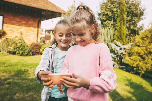 Dvě malé holčičky před jejich domem mluví na mobilním telefonu s přáteli nebo rodiči přes video link. — Stock fotografie