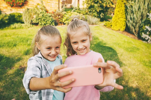 Dos adolescentes felices se ríen y se toman una selfie en un teléfono celular al aire libre. — Foto de Stock