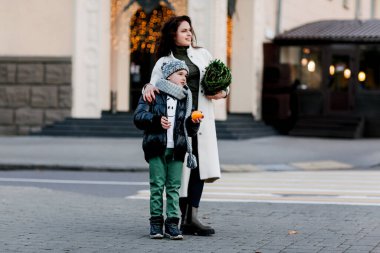 Neşeli bir çocuk ve genç annesi, bayram için küçük bir Noel ağacı aldıktan sonra sokakta kucaklaşıyorlar. Tatil hazırlığı, Noel alışverişi.