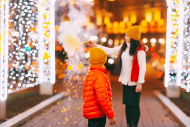 Anne ve oğlu yılbaşı ya da yeni yıl kutlamaları sırasında ellerinde renkli sis bombaları tutuyorlar.