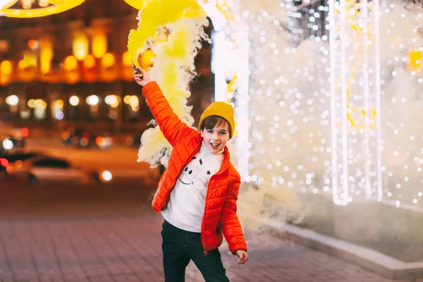 Seorang remaja laki-laki dengan bom asap di tangannya selama perayaan Natal atau Tahun Baru dengan latar belakang penerangan kota — Stok Foto