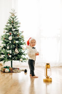 Noel ağacının arka planında Noel şapkalı küçük bir çocuk. Noel temalı resim, kartpostal.