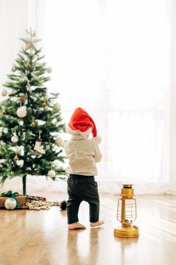 Noel ağacının arka planında Noel şapkalı küçük bir çocuk. Noel temalı resim, kartpostal.