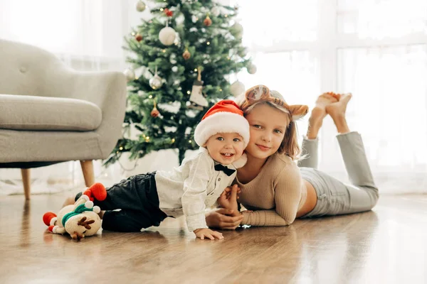 Portrait of two charming children in Christmas costumes next to the Christmas tree on the eve of the holidays. Festive mood, positive emotions. Christmas and New Year — Stock Photo, Image