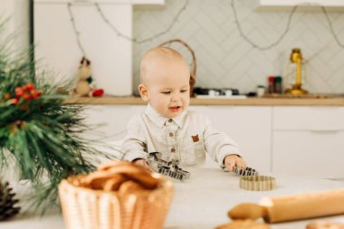 Kurabiye kesicilerle masada oturan mutlu bir çocuğun portresi. Tatil hazırlıkları, Noel dekorasyonu, Noel pastaları.