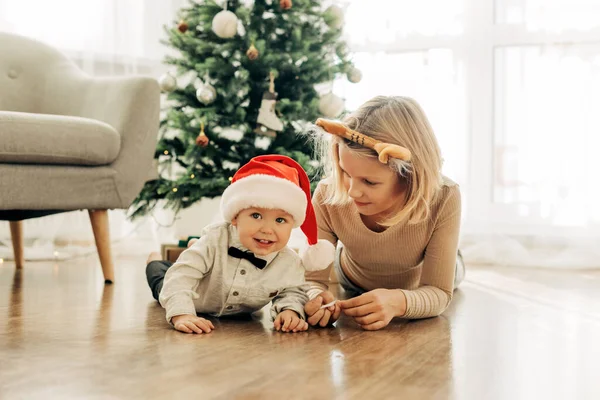 A charming girl and her younger brother play together on the floor next to the Christmas tree on Christmas or New Years Eve — Stock Photo, Image