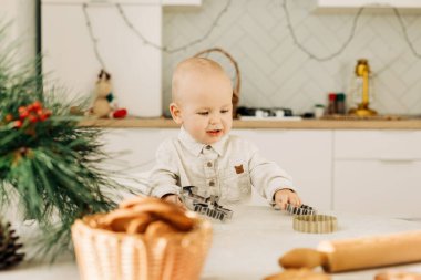 Kurabiye kesicilerle masada oturan mutlu bir çocuğun portresi. Tatil hazırlıkları, Noel dekorasyonu, Noel pastaları.