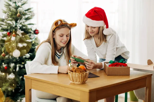 Due ragazze affascinanti scrivono saluti e auguri ad amici e parenti la vigilia di Natale o Capodanno vicino all'albero di Natale. — Foto Stock
