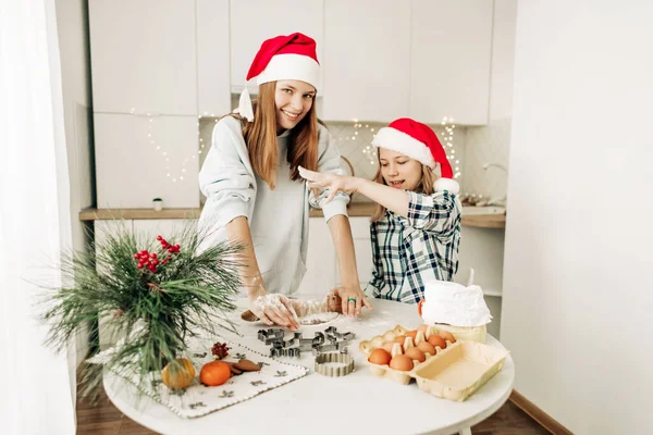 A cute girl helps her older sister prepare a Christmas dessert, the girls bake cookies and gingerbread. Christmas atmosphere, preparation for the holiday — Stock Photo, Image