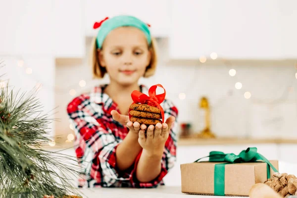 Un primer plano de una galleta atada con una cinta roja en las manos de una chica. Preparación para Navidad o Año Nuevo, galletas y regalos de Navidad —  Fotos de Stock