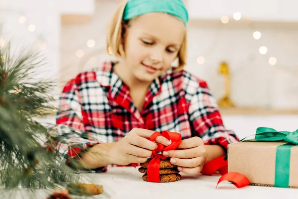 Una chica bonita decora galletas con una cinta roja brillante, prepara un dulce para los huéspedes en Navidad o Nochevieja — Foto de Stock