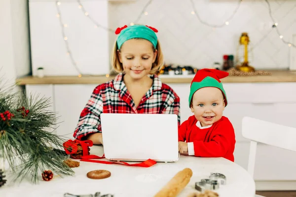 Brother and sister are sitting in the kitchen and congratulating their grandparents on Christmas and New Year via video link. Remote celebration of the online Christmas holiday — Stock Photo, Image