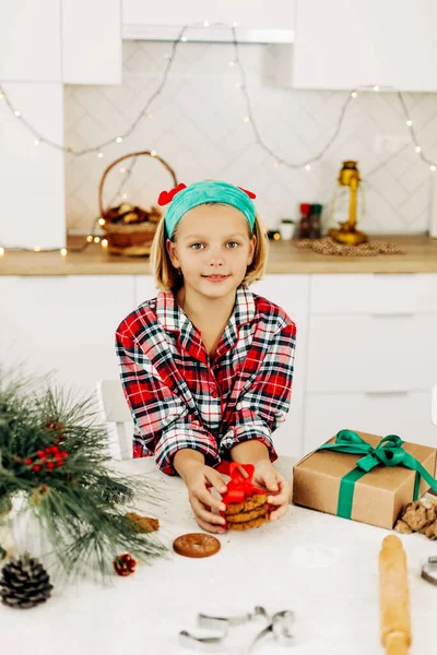 Una chica bonita decora galletas con una cinta roja brillante, sonrisas y sueños de celebrar la Navidad o Año Nuevo — Foto de Stock