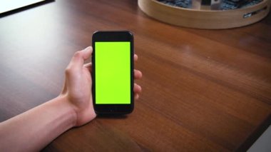 Erkek elinin modern akıllı telefonu dikey pozisyonda tutması, yeşil boş ekran. Masadaki iş için mobil başvuru formu. Metin için uzayı kopyala