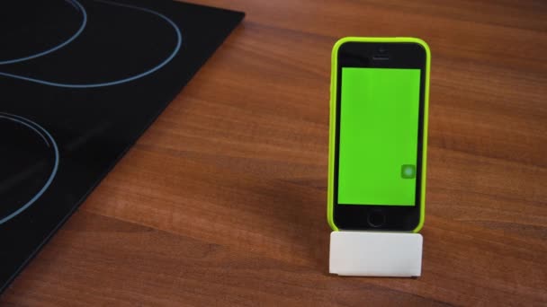 スタンド 緑の空の画面上の垂直位置に近代的なスマートフォン 自宅での仕事のためのモバイルアプリケーション コンロ付きのキッチンテーブル テキストのためのスペースをコピー — ストック動画