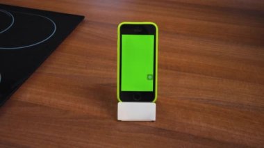 Modern akıllı telefon dikey pozisyonda, yeşil boş ekran. Evde çalışmak için mobil başvuru formu. Hob 'la mutfak masası. Metin için uzayı kopyala