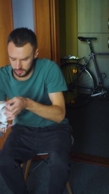 Adam müzik dinlemek için kablosuz kulaklık hazırlıyor. Oturma odasında sakallı, beyaz bir adam. Dikey video. Müzik ve sesli kitapları dinleyebilirsin. Boşluğu kopyala.