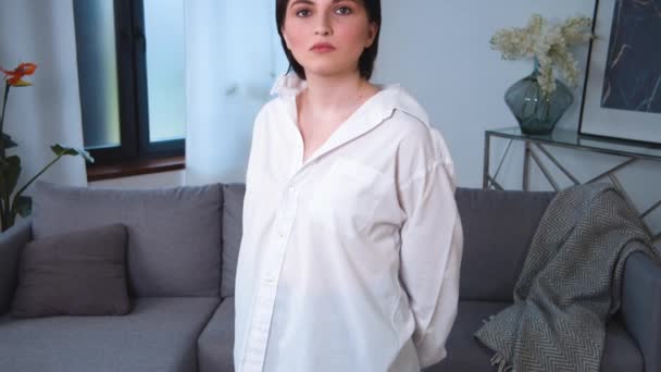 Wanita hamil Kaukasia potret melihat kamera dan perut. Berdiri di ruang tamu apartemen. Gadis muda yang percaya diri, berambut pendek. Kamera turun. — Stok Video
