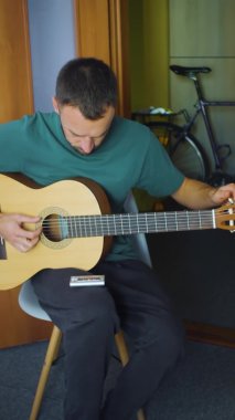 Evdeki beyaz müzisyenin dikey portresi. Erkekler salonda gitar çalar. Günlük giyinmiş Avrupalı müzisyen bir şarkı söylüyor