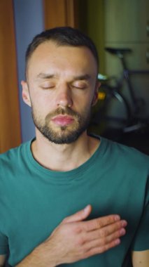 Elini kalbe koyan adamın dikey portresi. Genç beyaz erkek kameraya sevgi ve destek kavramı gösteriyor.