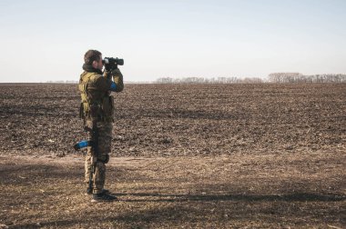 Kyiv, Ukrayna - 03 / 23 / 2022: Rus-Ukrayna savaşı sırasında düşman mevzilerine dürbünle bakan Ukraynalı bölge savunma askeri