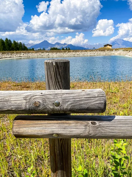 Beautiful view over a wooden fence between wooden fence posts, framed by a tall Alps Pine tree mountain forest backdrop. Country basic handmade rural wooden fence near lake, blue sky backdrop