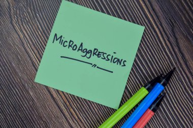 Microaggressions write on sticky notes isolated on Wooden Table. clipart