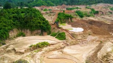 Kamyonların ve kazıcının altın madenciliğiyle ilgili açık bir çukurdaki hava görüntüsü. Merkez Sulawesi, Endonezya, 29 Mart 2022
