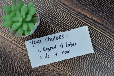 Concept of your choices - regret it later or do it now write on sticky notes isolated on Wooden Table.