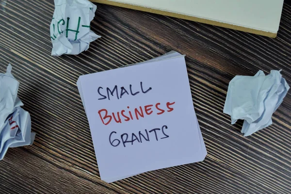 Concept of Small Business Grants write on sticky notes isolated on Wooden Table.