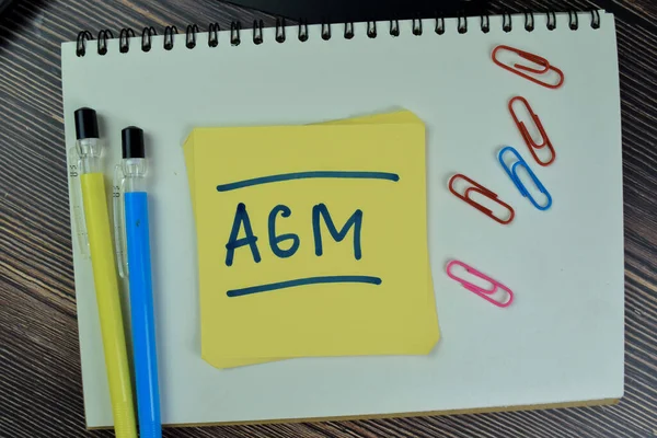 Concept of AGM - Annual General Meeting write on sticky notes isolated on Wooden Table.
