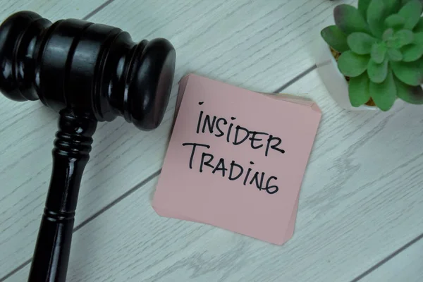 Concept of Insider Trading write on sticky notes with gavel isolated on Wooden Table.