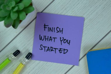 Concept of Finish What You Started write on sticky notes isolated on Wooden Table.