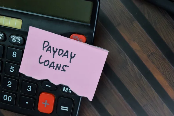 Concept of Payday Loans write on sticky notes with calculator isolated on Wooden Table.