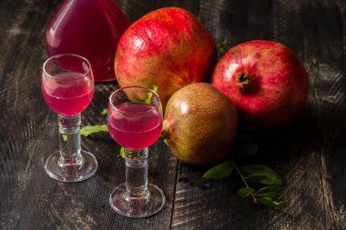 Ev yapımı nar likörü mü? Siyah ahşap zemin üzerinde nar ve içinde likör olan iki bardak.