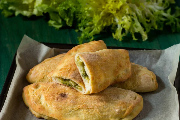 Fırında parşömen kağıdıyla pişirilmiş panzerotti ve grana padano. Yeşil ahşap arka planda Panzerotti yakın plan ve arka planda pürüzsüz ve kıvrımlı hindiba desenleri