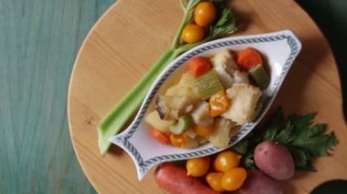 Patates, kereviz ve havuçla haşlanmış morina balığı. Tabağın yakın çekimi pişmeye hazır, yeşil ahşap arka planda.