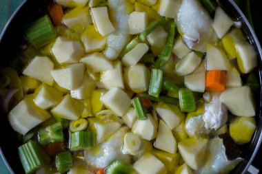 Patates, kereviz ve havuçla haşlanmış morina balığı. Tavanın yakın çekimi pişmeye hazır, yeşil ahşap arka planda.